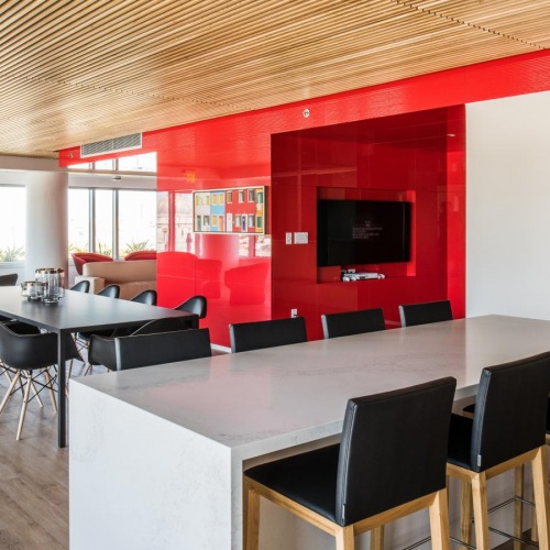 Studios in San Francisco CA - Trinity Place at 33 8th - Clubhouse Lounge Space with Red Accent Walls, TV, Couches, Tables with Chair, and City Views Through Large Windows