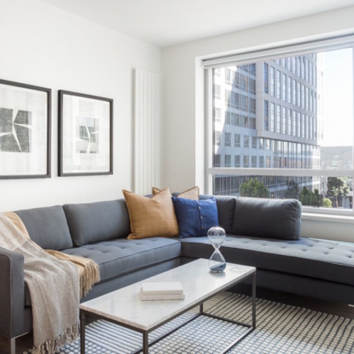 Luxury Apartments in San Francisco, CA - Trinity Place at 33 8th - Well-lit Living Space with a Couch, a Coffee Table, a Side Table, Art, White Walls, and a Large Window